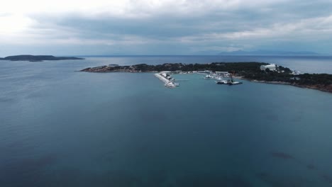 Tiro-Panorámico-De-Drone-De-ángulo-Alto-De-La-Hermosa-Península-Pequeña-Con-Puerto-Deportivo-Para-Yates-Durante-Una-Tranquila-Tarde-Nublada-En-El-área-De-Laimos-En-Vouliagmeni,-Grecia-|-4k