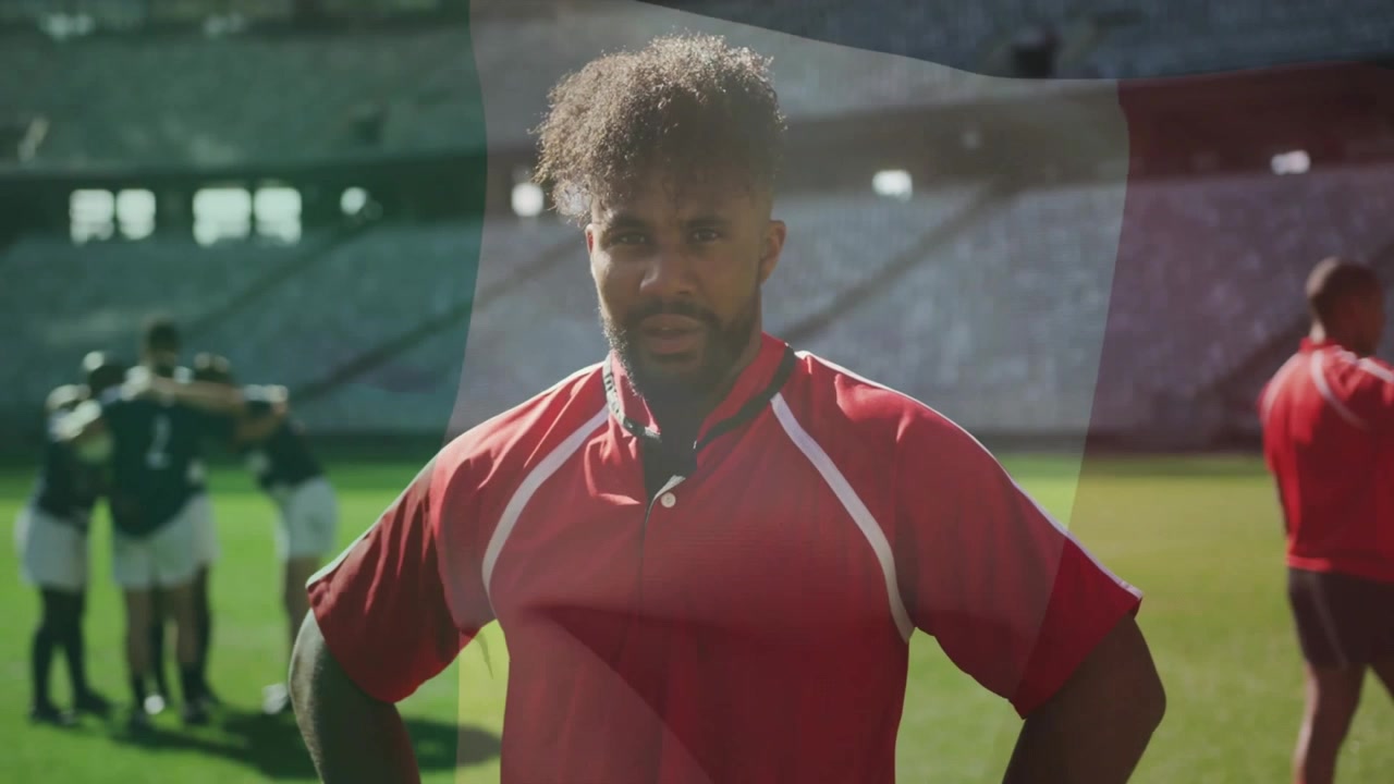 La telecamera zooma su un atleta in rosso che si concentra sul campo sportivo, avversari che si raggruppano, con una bandiera in sovrimpressione che sventola