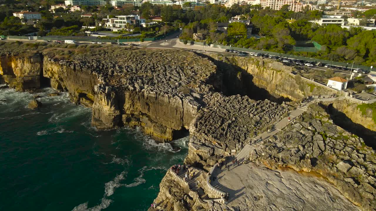 Aerial drone video orbiting around a famous tourist attraction called devils mouth or Boca do Inferno in Portugal coastline in Cascais during a sunny day, with turquoise waves hitting the tall cliffs