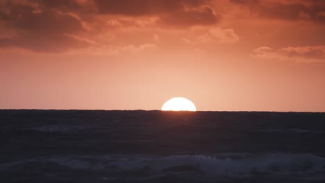 gentle waves move rhythmically under a glowing sunset, illuminating the sea with hues of orange and blue.