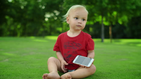 toddler sitting on grass in summer field. closeup little boy holding smartphone