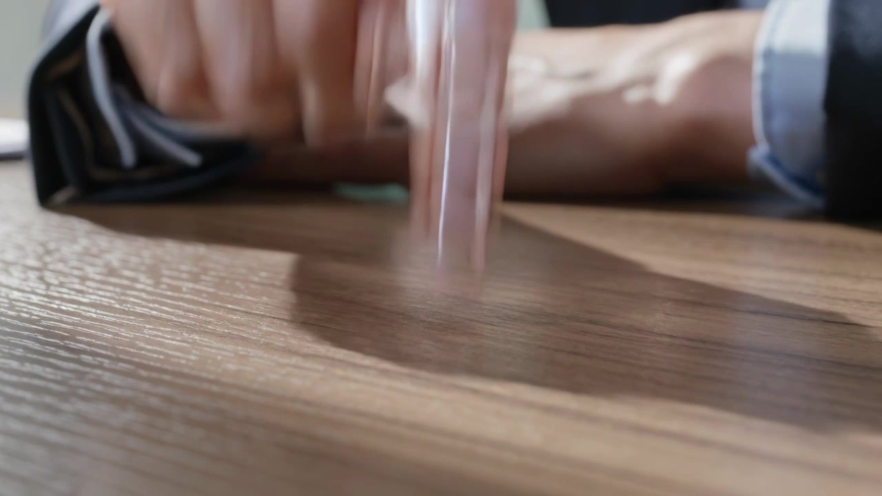 Resting woman's right hand tapping tip on wood table in office, showing pink nails, sleeve, shadow