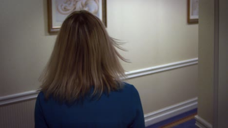 young blonde woman in blue dress walking on hallway corridor at guest hotel