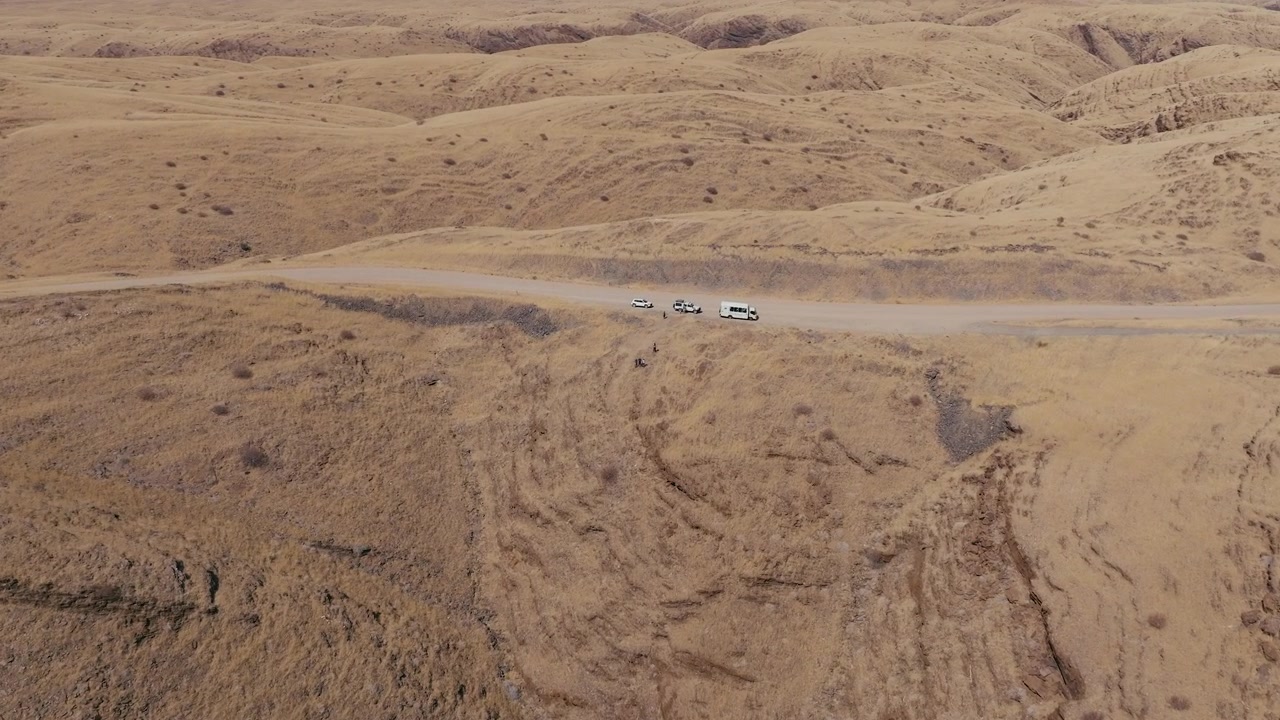 High angle aerial shot of offroad vehicles parked on a remote dirt road in the vast Namibian desert landscape. Ideal for travel documentaries and adventure tourism content.