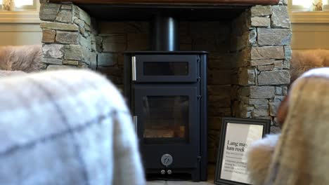 sideways movement focusing on a brand new black metal logburner fire in a custom built stone cabin lodge with 2 cosy arm chairs as foreground in front of the fire