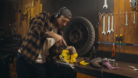 confident guy mechanic in headphones listens to music and works while drinking soda from his workshop studio