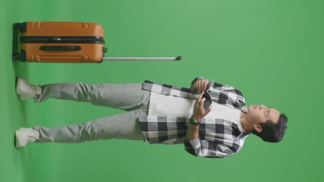 full body of asian male traveler with luggage looking at the passport and looking around while standing in the green screen background studio