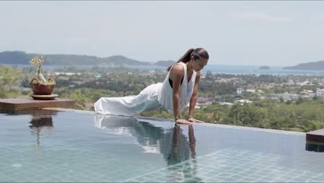 mujer relajada haciendo ejercicio de cobra bebé cerca de la piscina contra un hermoso paisaje