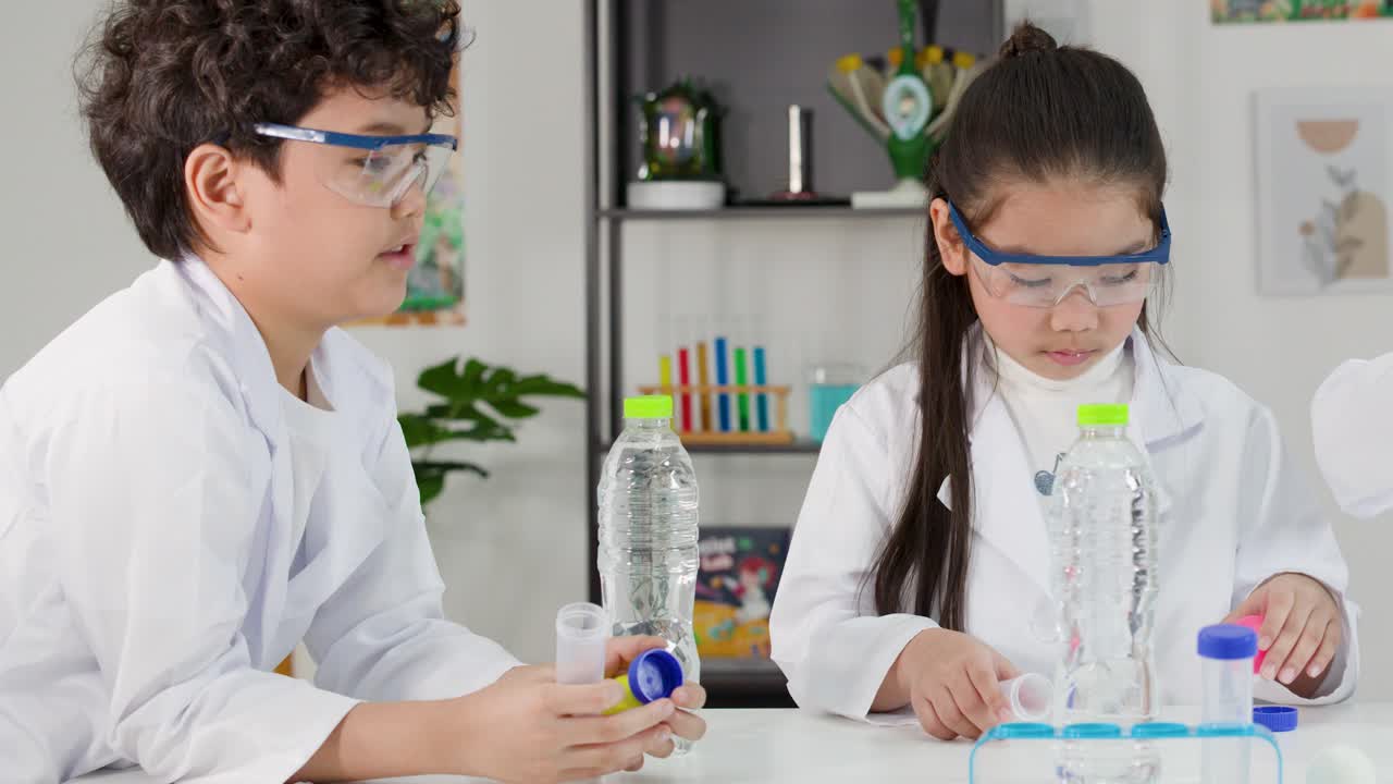 Two Asian children in lab coats perform a Bernoulli's principle science experiment in a classroom