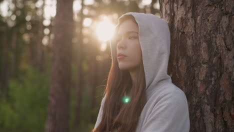 woman in a hoodie standing in a forest looking at the sunset