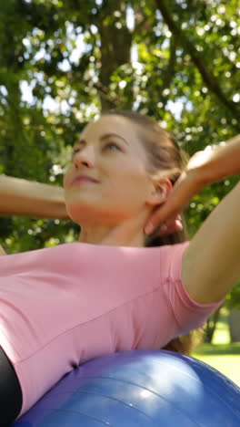 fit woman doing sit ups on exercise ball in the park