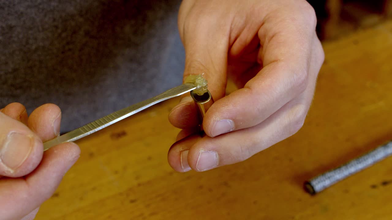 Crafstman gluing silver clasp of bracelet on workshop table, close up view