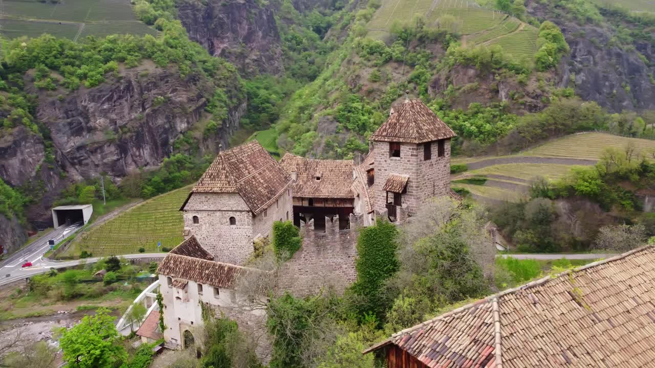 Drone circles Roncolo Castle near Bolzano, with a tunnel leading into the mountains in the backdrop