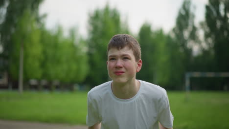 a young boy focuses intently as he heads a soccer ball away in a grassy field, with a blurred view of a goalpost and lush trees in the background