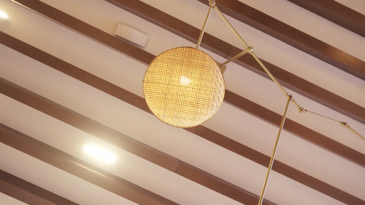 Low angle orbiting shot of luxury woven rattan pendant lighting on a designer wood slat ceiling in a boutique hotel lobby or upscale commercial interior