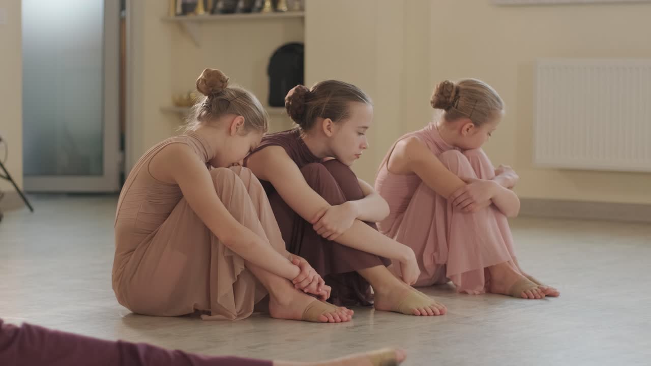 un grupo de jóvenes estudiantes de ballet con ropa de baile negra practicando posiciones en un amplio estudio de ballet con pisos de madera y barras montadas en la pared. expresiones enfocadas y movimientos sincronizados.