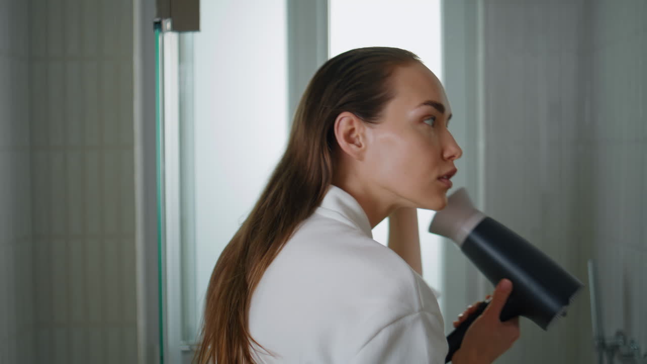 Pretty girl using hairdryer in home bathroom closeup. Attractive model preparing