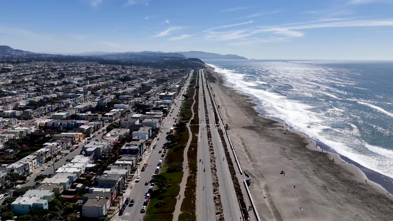 High-angle drone view of Ocean Beach with surf lines, pedestrian paths, and residential blocks along San Franciscoâ€™s Great Highway on a sunny day.