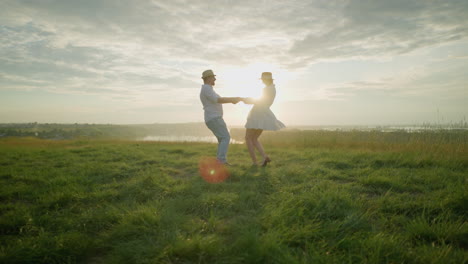 two lovebirds spin lovingly on a grassy hill at sunset, beside a serene lake. the man, dressed in a white shirt, hat, and jeans, embraces his wife, who is wearing a flowing white dress