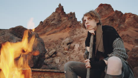 woman sitting by campfire in post apocalyptic world