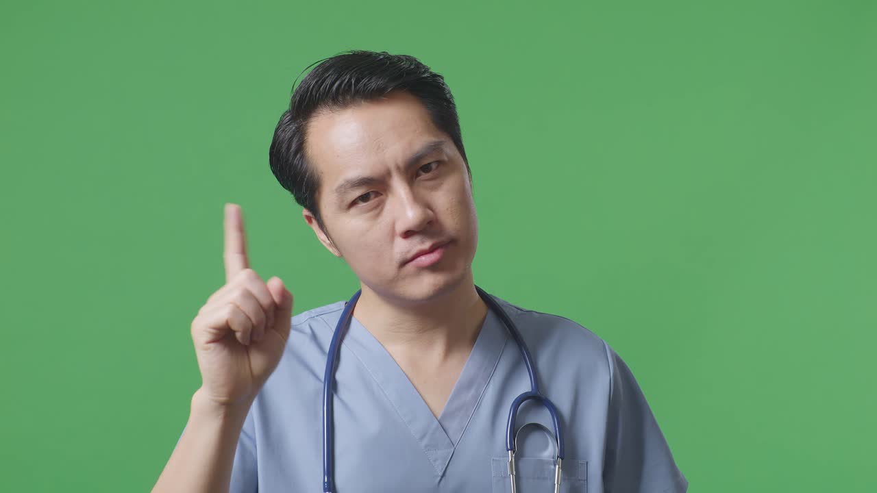 병원 에서 녹색 스크린 배경 에 서 있는 동안 어떤 몸짓 도 보여주지 않는 스테토스코프 를 들고 있는 아시아 남자 의사 의 근접 사진