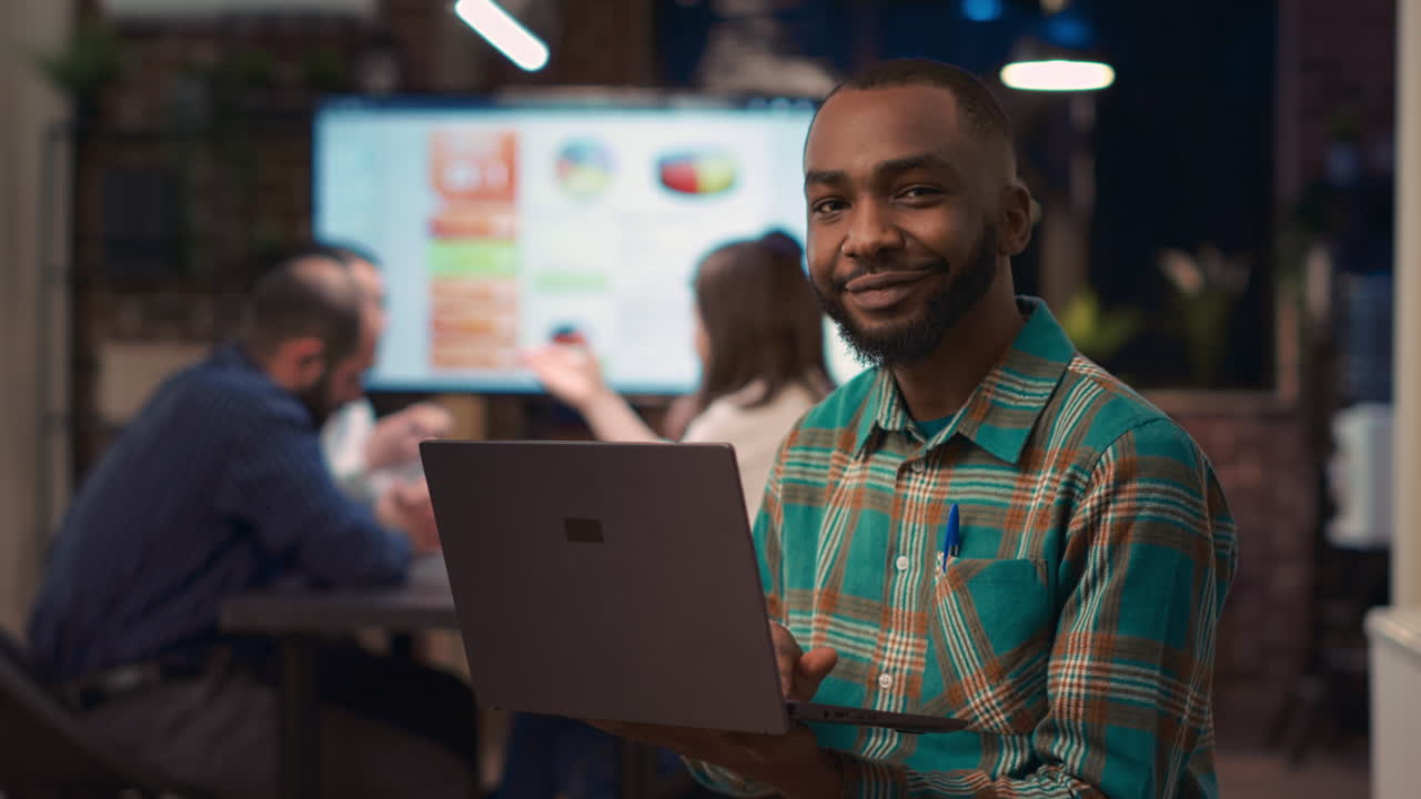 African american employee working on laptop, looking at camera
