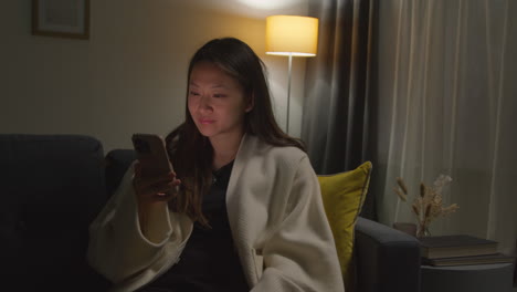 Woman Spending Evening At Home Sitting On Sofa With Mobile Phone Scrolling Through Internet Or Social Media 2