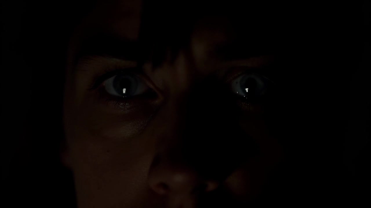 Sich erweiternde Augen einer weiblich dargestellten Person, die auf sich aus dem Frame bewegendes Licht im dunklen Raum reagiert und eine Träne bildet