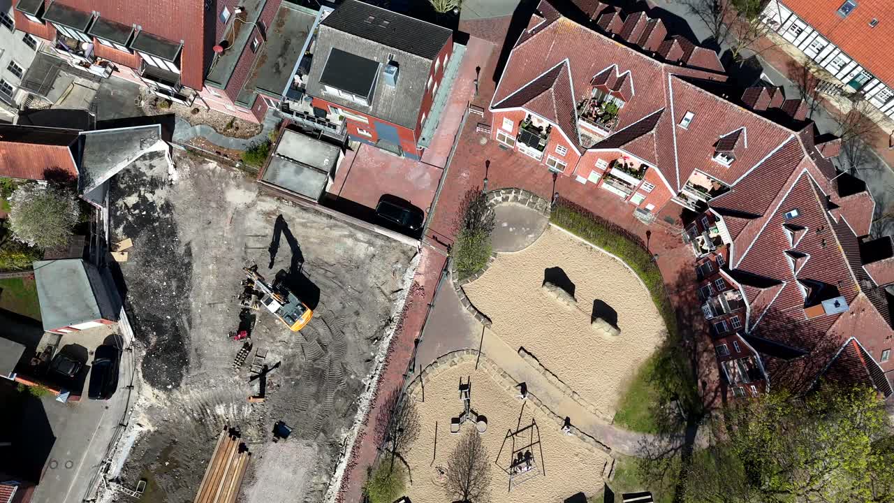 Aerial top down construction site with crane beside playground of american town. Sunny day in small city. Red brick apartment houses and parking cars.