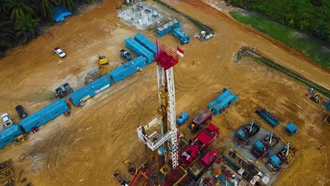 Cinematic-Drone-Shot-of-Onshore-Drilling-and-Workover-Rig-structure-and-Rig-equipment-for-oil-exploration-and-exploitation-in-the-middle-of-jungle-surrounded-by-palm-oil-trees-during-sunset-time