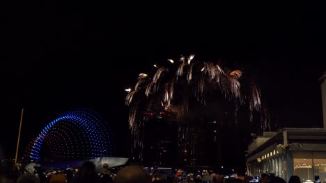 unrecognisable crowd of people watch firework and drone show celebrations over an urban skyline