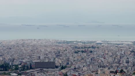 Teleobjetivo-Drone-Aéreo-Sobrevuela-La-Ciudad-De-Atenas,-Día-Nublado-Y-Cambiante-Vista-Panorámica-Del-Mar-Y-Los-Edificios