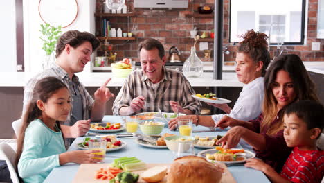 Multi-Generation-Family-Enjoying-Meal-Around-Table-At-Home