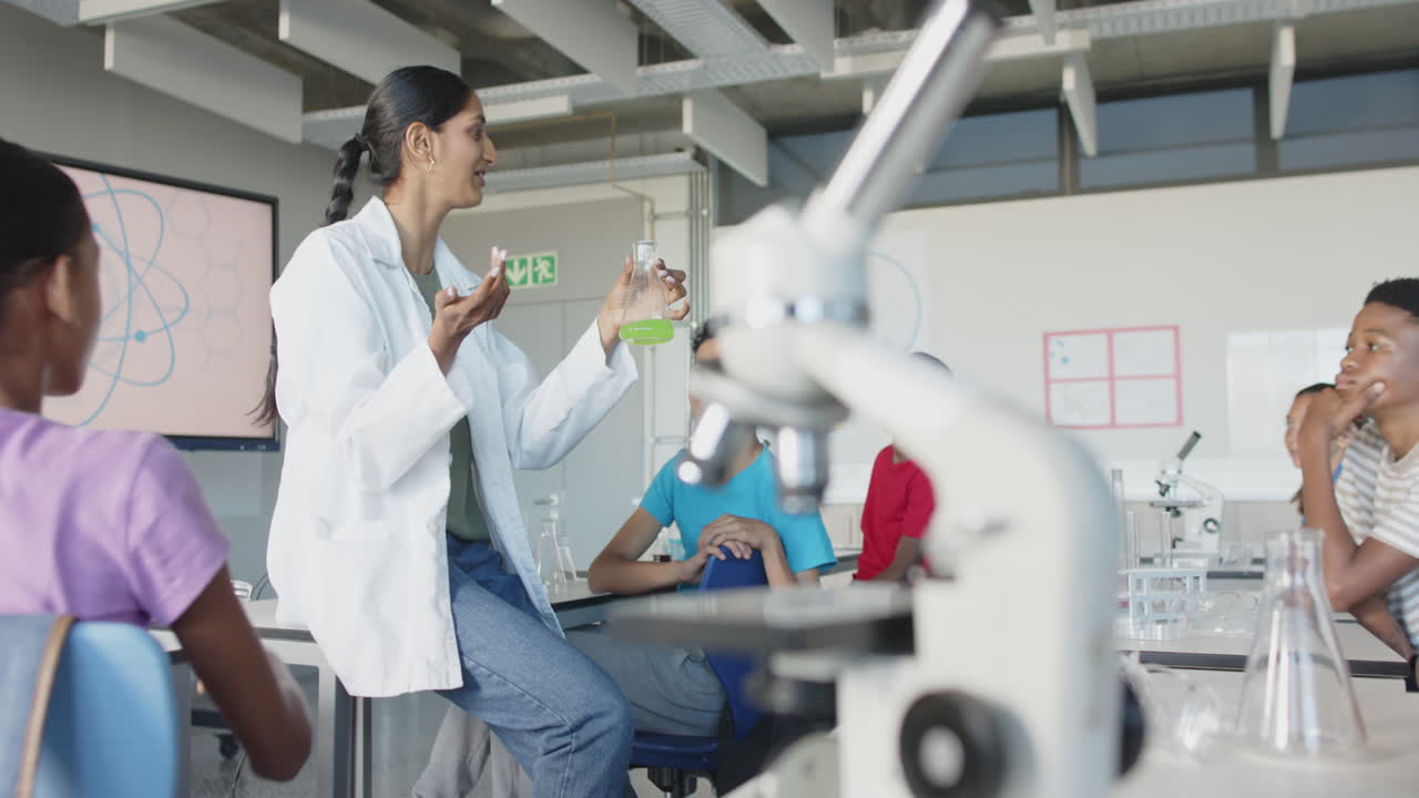 In school, teacher showing green liquid in beaker to engaged students in classroom