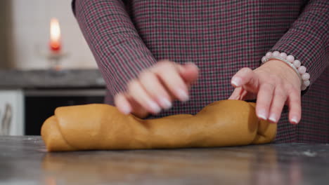 partial view of chef with bracelet on left hand adjusting and kneading fresh dough on kitchen counter with red candle burning in background, modern kitchen ambiance