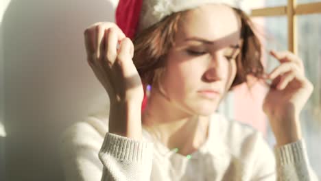 woman wearing a santa hat looking sad by a window