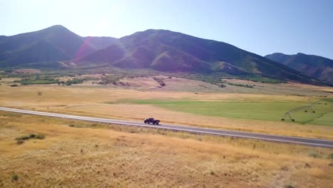 a drone follows a pickup truck on a lonesome road that runs into a valley up into the mountain range on a clear summer day