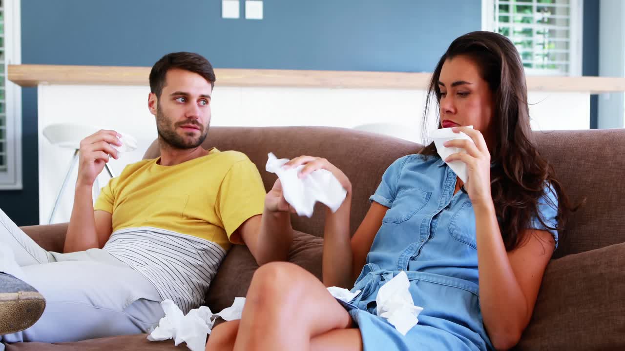 Couple blowing their nose in tissue in living room at home