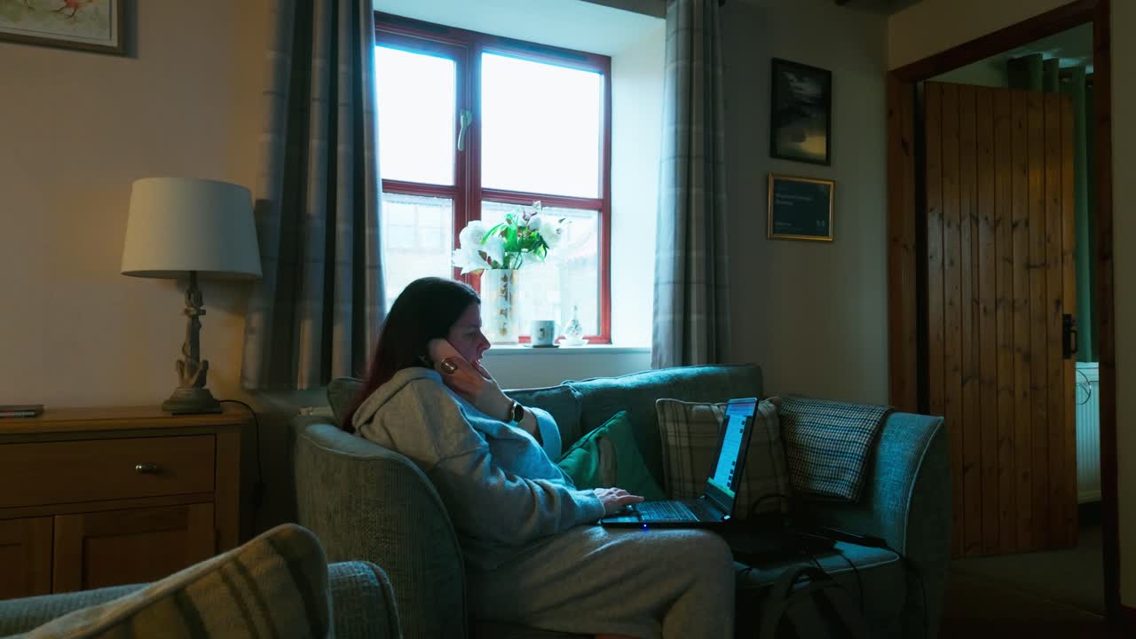 여성이 소파에서 휴식을 취하고 모바일 스마트폰을 사용하고 노트북에서 일하고 있습니다.