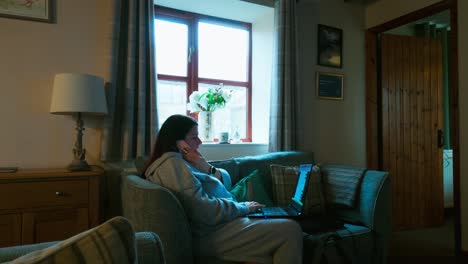 woman relaxing on a sofa using her mobile smartphone and working on her laptop