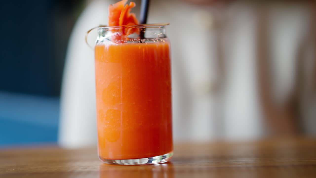 Donna che beve succo di carota con una cannuccia, al ristorante. Verticale