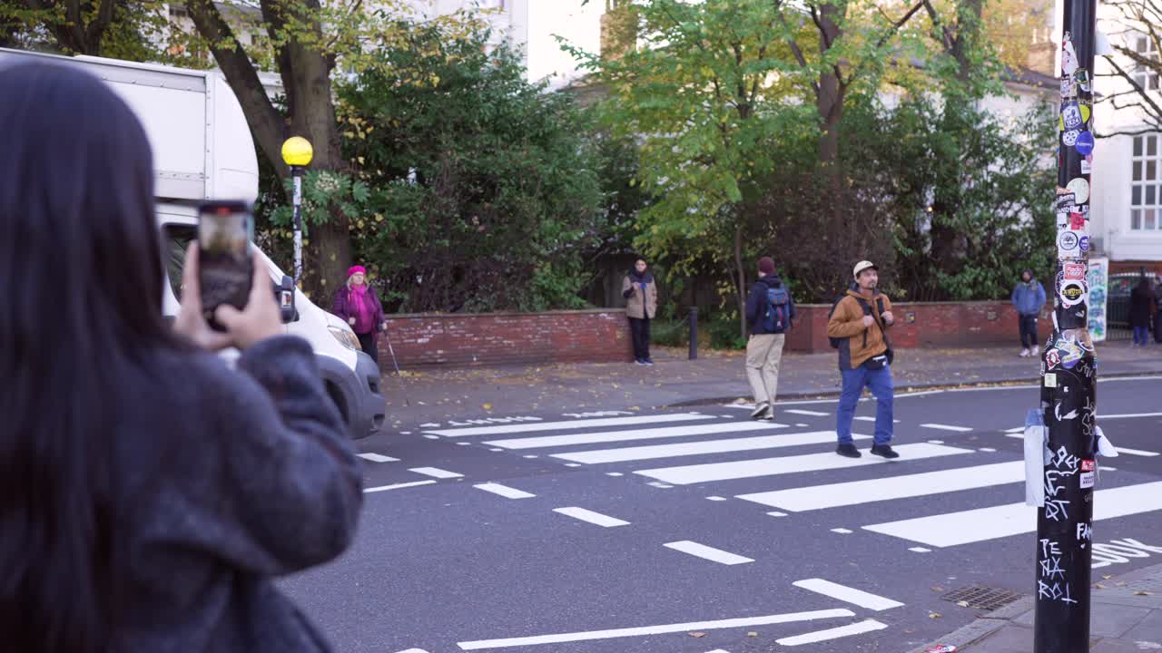 Tourists on Abbey Road in London recreate the iconic Beatles crossing, capturing photos of themselves on the road