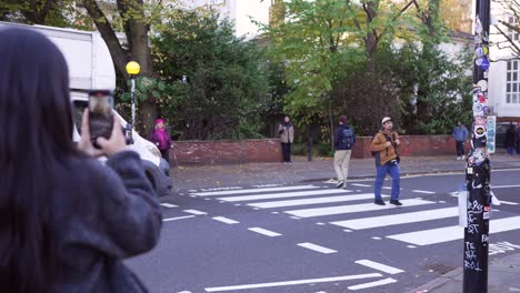 tourists on abbey road in london recreate the iconic beatles crossing, capturing photos of themselves on the road