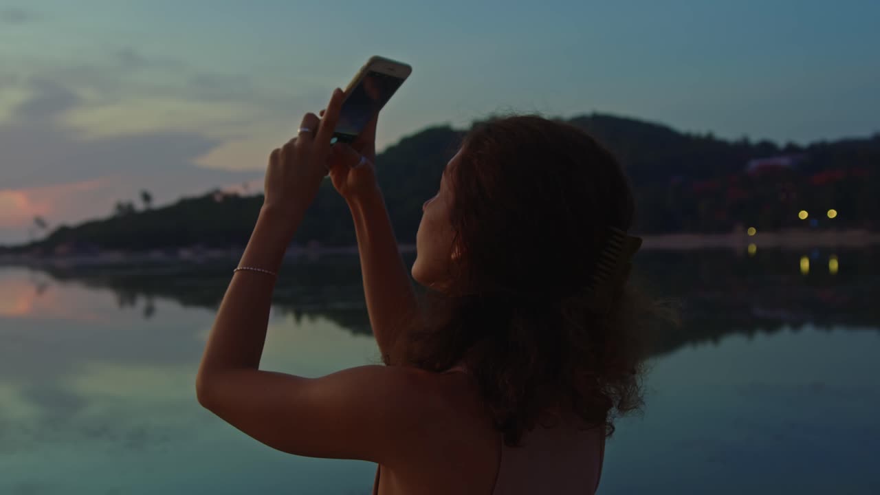 mujer tomando una foto de la puesta de sol en la playa