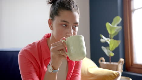 una adolescente biracial pensativa sentada en casa bebiendo té, copiando el espacio, en cámara lenta