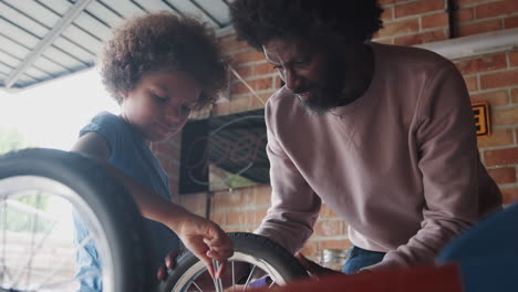 Primer-Plano-En-ángulo-Bajo-De-Un-Padre-Negro-De-Mediana-Edad-Ayudando-A-Su-Hijo-A-Colocar-Una-Rueda-En-Su-Kart-De-Carreras