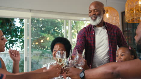 Multi-Generation-Family-Sitting-Around-Table-Doing-Cheers-With-Wine-Before-Meal-At-Home-Together