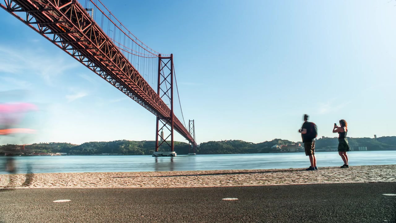 Timelapse en plano medio de personas y bicicletas en una acera junto al río en Lisboa