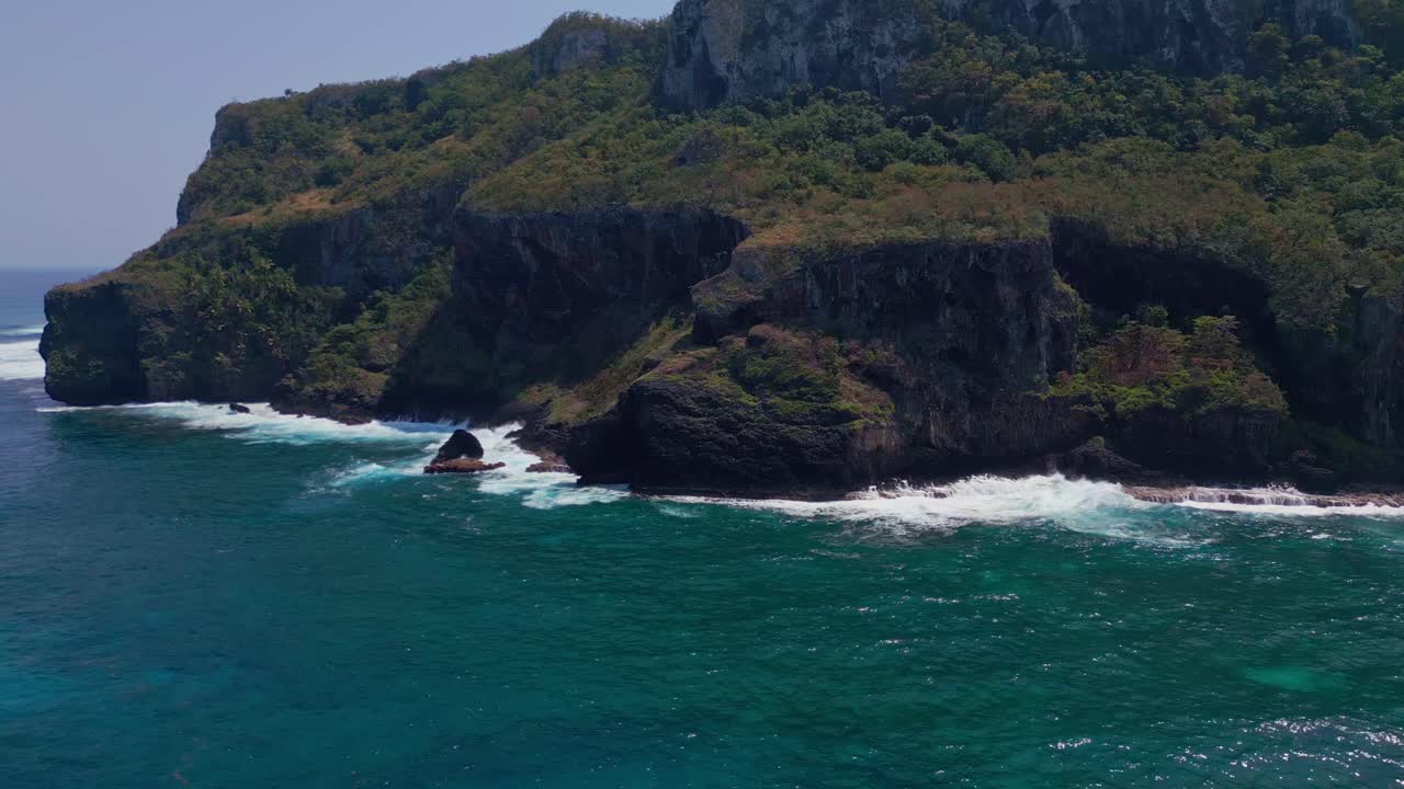Drone panorama shot of green mountain and crashing waves of Caribbean Sea against rocky coastline - Blue sky and sunlight at Cabo Samana, Dominican Republic