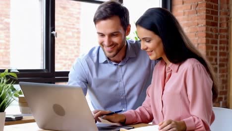 Two businessperson with laptop at desk in open plan office collaborating on project together